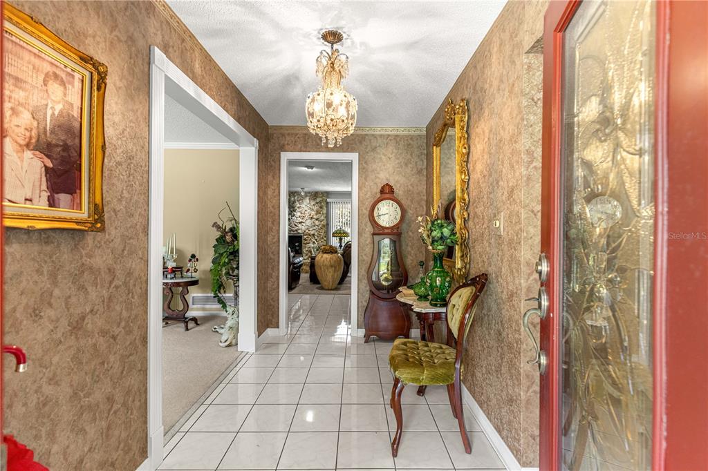 A tiled entryway features a crystal chandelier, a grandfather clock, and wallpapered walls — 3963 SE 15TH STREET, OCALA, FL