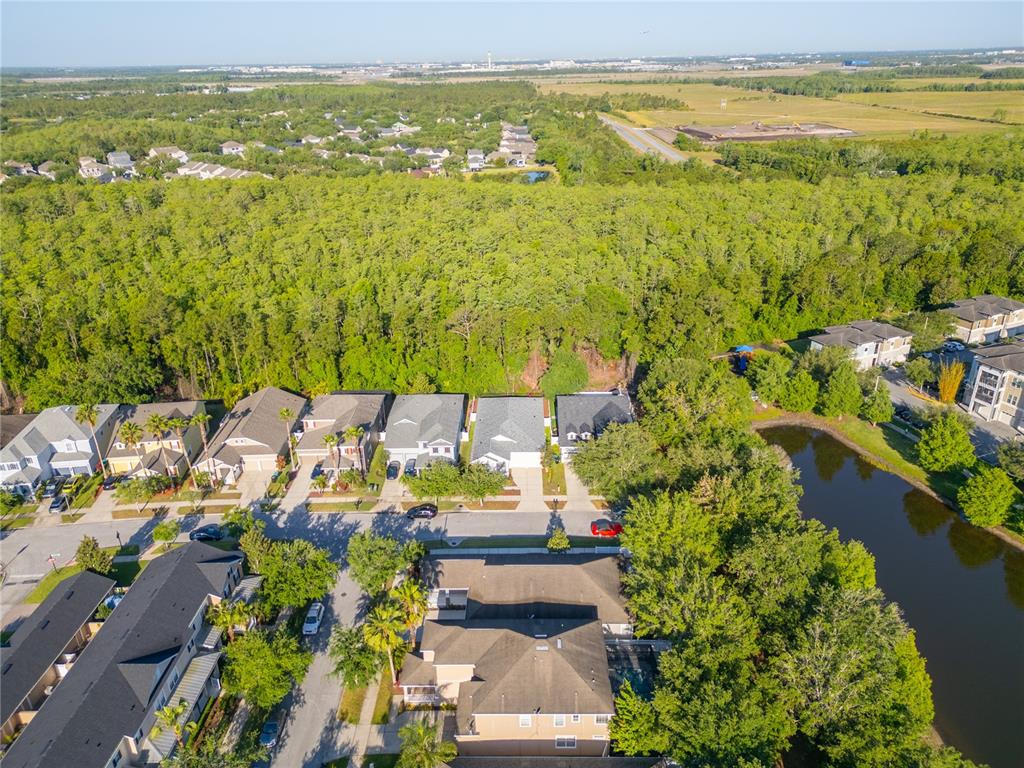 An aerial view shows a suburban neighborhood with houses, a pond, and surrounding forest — 9516 PICCADILLY SKY WAY, ORLANDO, FL