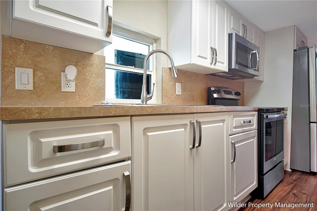 A kitchen features white cabinetry, stainless steel appliances, a tiled backsplash, and wood-look flooring — 26 FOREST DRIVE UNIT 32 A, DAVENPORT, FL