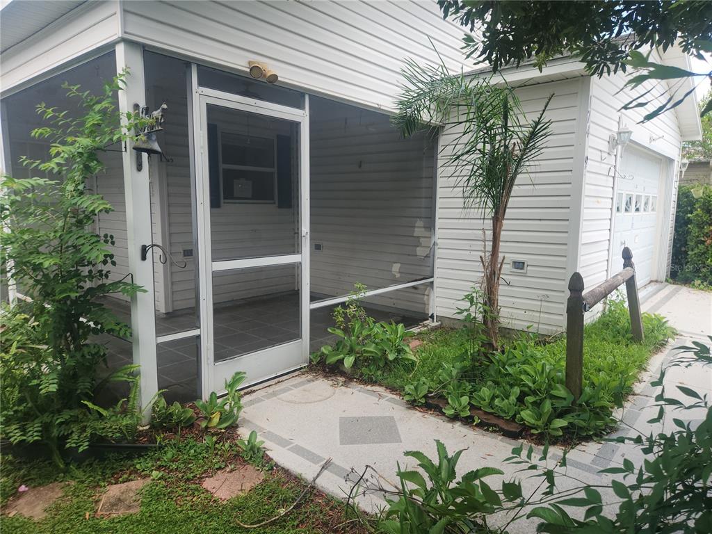 A screened-in porch with tiled flooring sits adjacent to a white-sided house and garage — 17449 SE 81ST NEWBERRY COURT, THE VILLAGES, FL