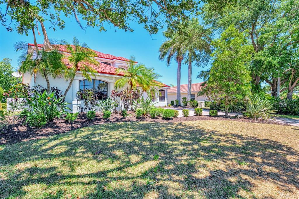 A white house with a red tile roof surrounded by palm trees and landscaping — 5684 EASTWIND DRIVE, SARASOTA, FL