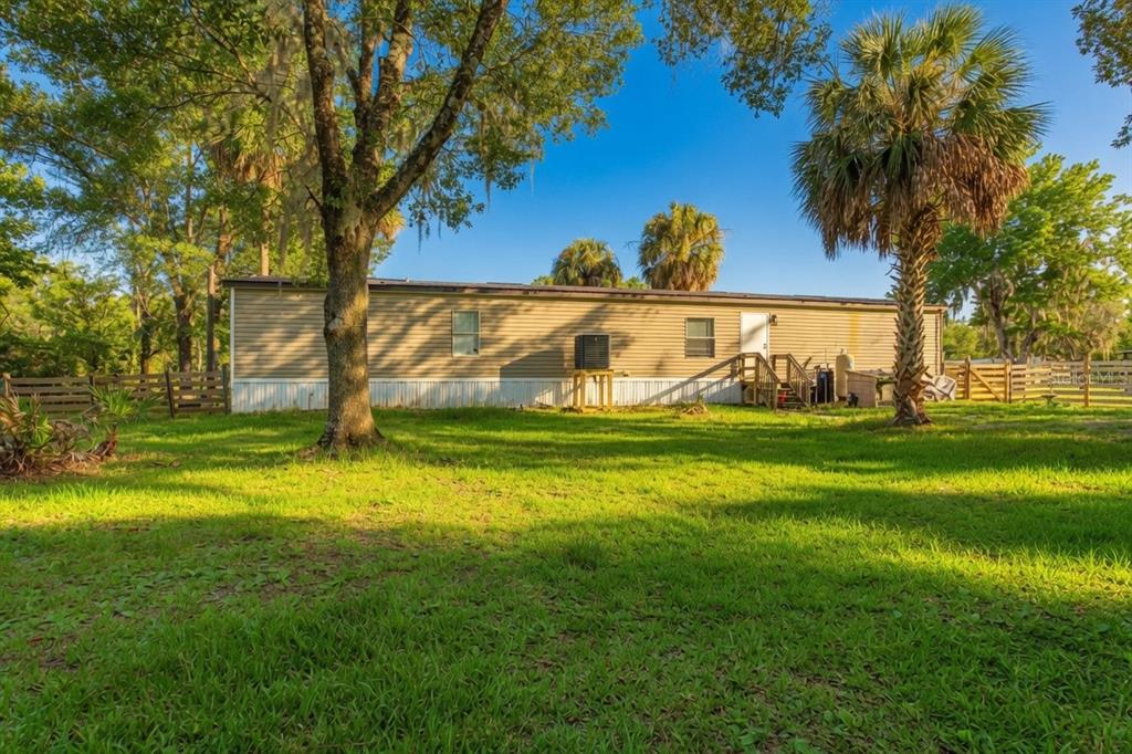 A tan mobile home sits on a grassy lot surrounded by trees and a wooden fence — 935 S CRYSTAL GROVE POINT, HOMOSASSA, FL