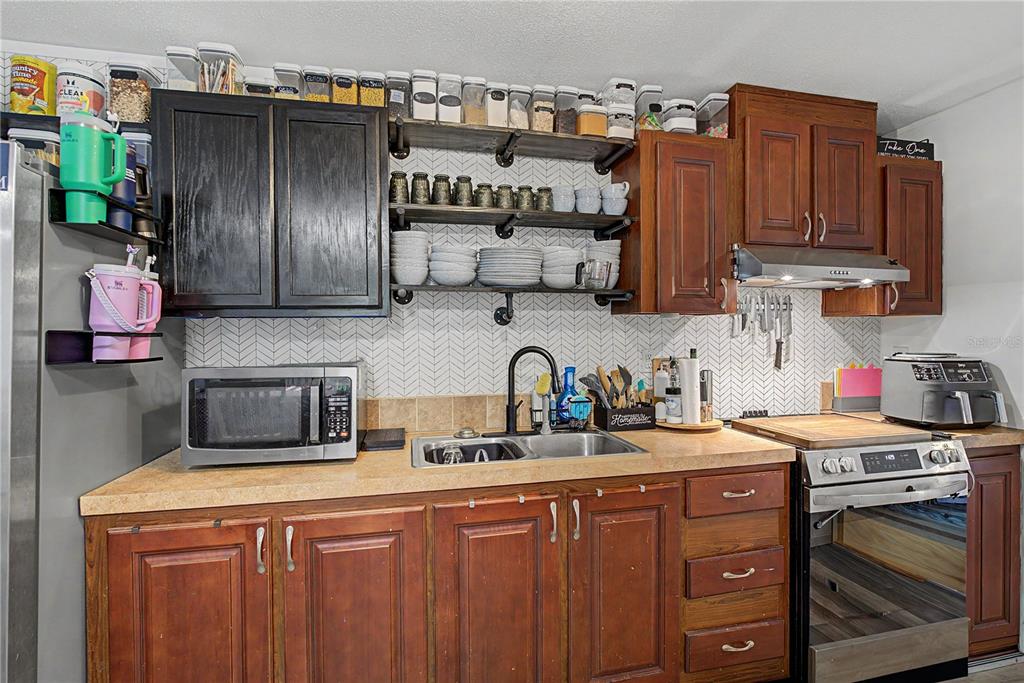 A kitchen features wood cabinets, open shelving, a herringbone backsplash, and stainless steel appliances — 935 S CRYSTAL GROVE POINT, HOMOSASSA, FL