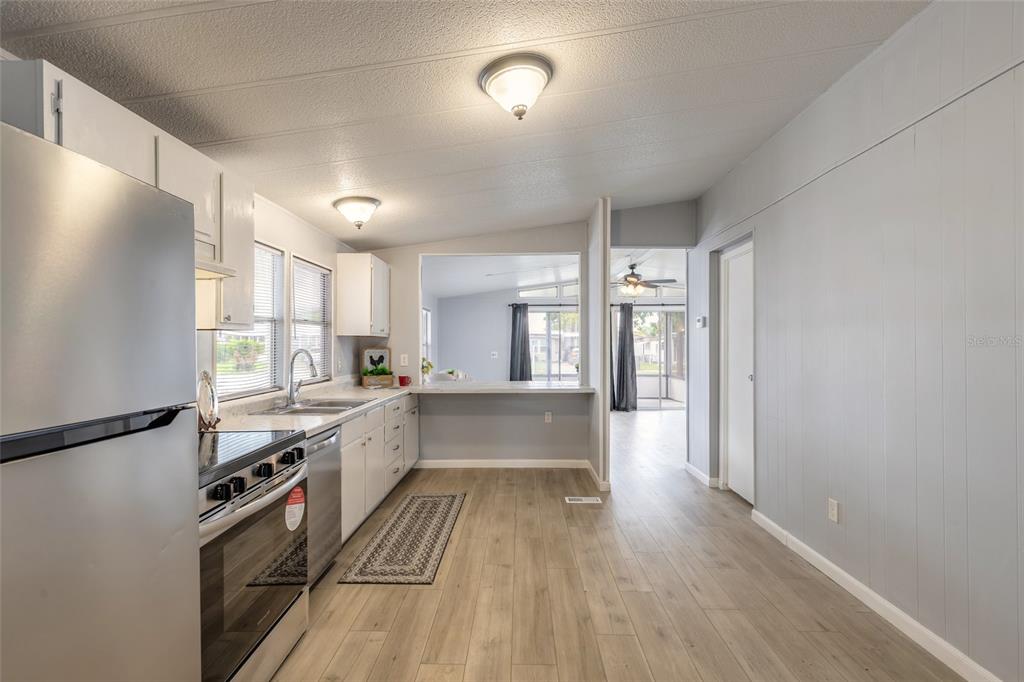 A kitchen with stainless steel appliances, light wood-look flooring, and a pass-through window — 103 ALOHA TERRACE, PORT ORANGE, FL