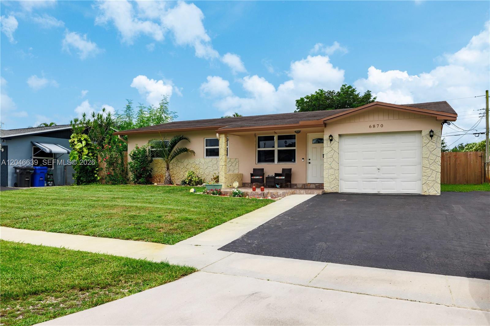 A single-story house with a tan exterior, stone accents, a garage, and a front lawn — 6870 Pershing St, Hollywood FL 33024, HOLLYWOOD, FL