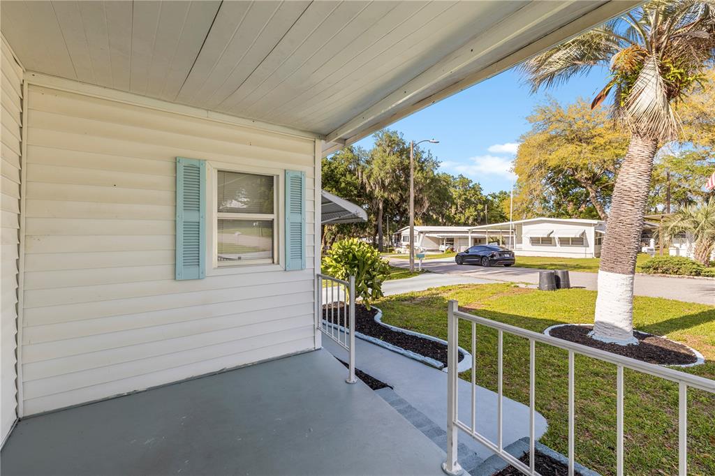 A covered porch with white siding, light blue shutters, and a metal railing overlooks a yard — 6123 RIDGEWOOD DRIVE, ZEPHYRHILLS, FL