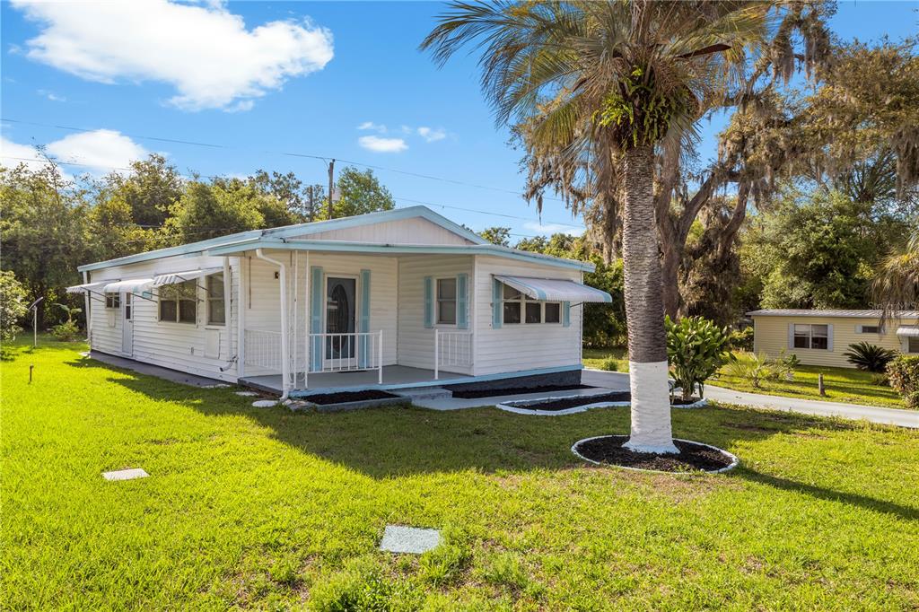 A white mobile home with a front porch and a palm tree in the yard — 6123 RIDGEWOOD DRIVE, ZEPHYRHILLS, FL