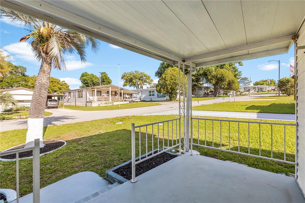 A covered front porch with a metal railing overlooks a residential street and palm tree — 6123 RIDGEWOOD DRIVE, ZEPHYRHILLS, FL