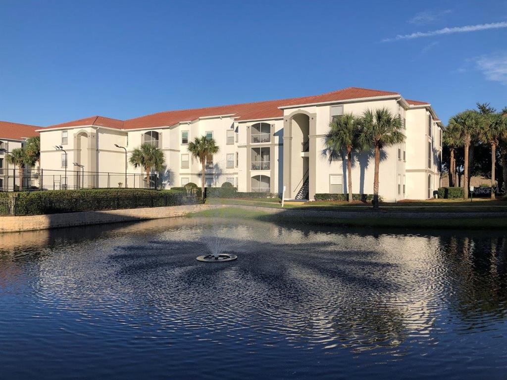 A multi-story apartment building with a red tile roof stands behind a pond with fountain — 2627 MAITLAND CROSSING WAY UNIT 304, ORLANDO, FL