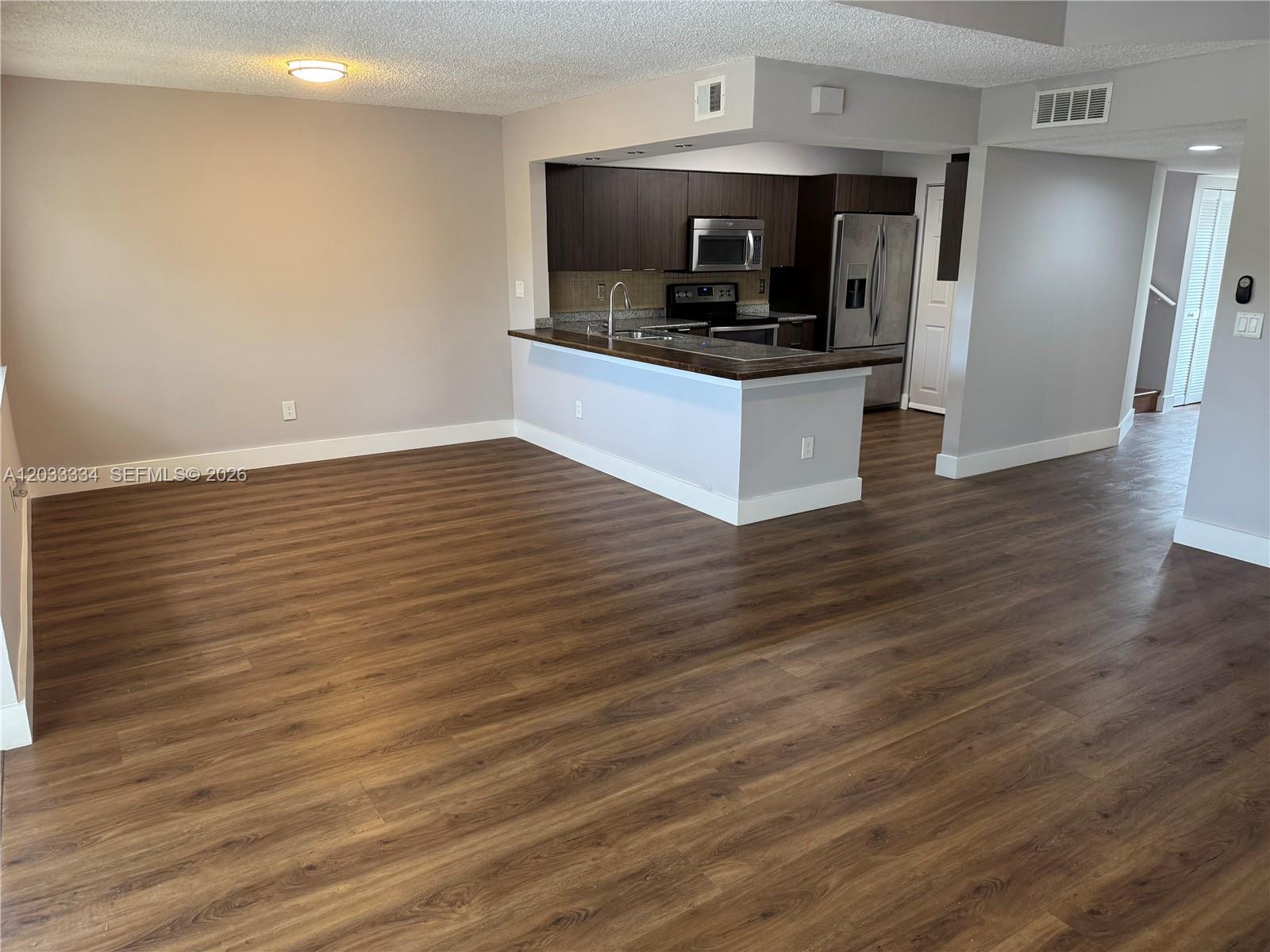 An open-concept living area features wood-look flooring and a kitchen with dark cabinetry — 11749 Terra Bella Blvd, Plantation FL 33325, PLANTATION, FL