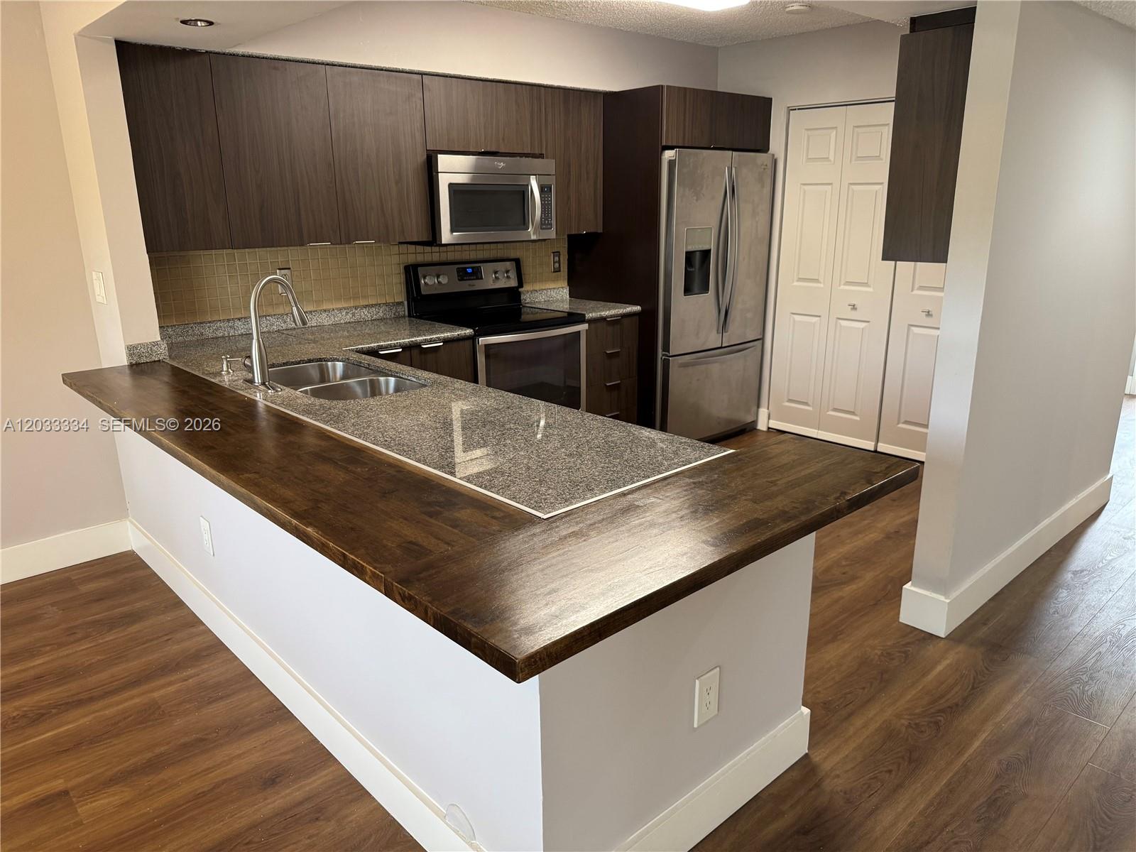 A kitchen features dark wood cabinets, granite countertops, stainless steel appliances, and wood-look flooring — 11749 Terra Bella Blvd, Plantation FL 33325, PLANTATION, FL