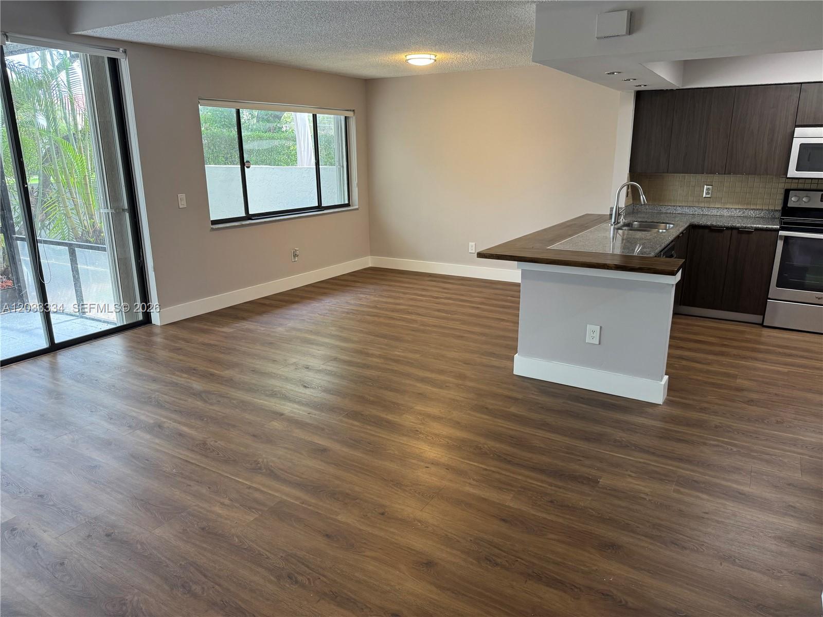 An open-concept living area features wood-look flooring, a kitchen island, and a sliding glass door — 11749 Terra Bella Blvd, Plantation FL 33325, PLANTATION, FL