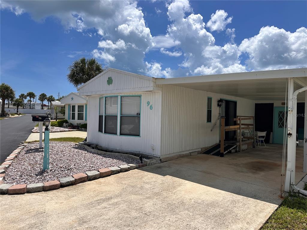 A white mobile home with a carport and a gravel front yard under a blue sky — 96 MERRIMAC DRIVE, FLAGLER BEACH, FL