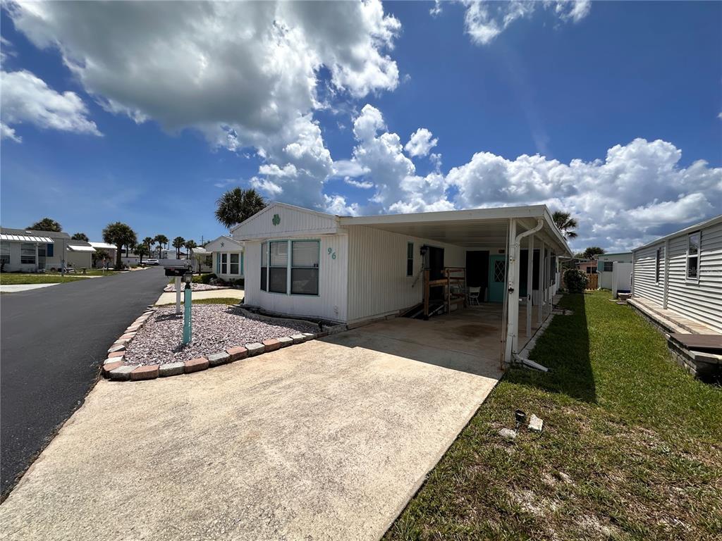 A white mobile home with a carport and a gravel front yard under a blue sky — 96 MERRIMAC DRIVE, FLAGLER BEACH, FL