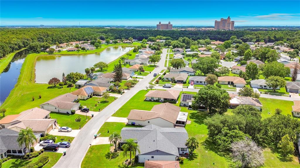 An aerial view shows a suburban neighborhood with houses, a pond, and distant large buildings — 5518 SANDY HILL DRIVE, ORLANDO, FL