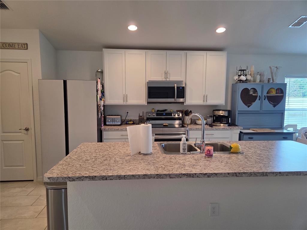 A kitchen features white cabinets, stainless steel appliances, a kitchen island, and granite-look countertops — 4570 PENKERT PLACE, LAKELAND, FL