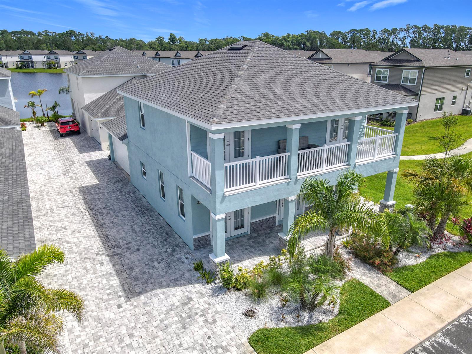 An elevated light blue two-story house features a paved driveway, white railings, and palm trees — 3121 Portofino Boulevard, FL 32168, FL