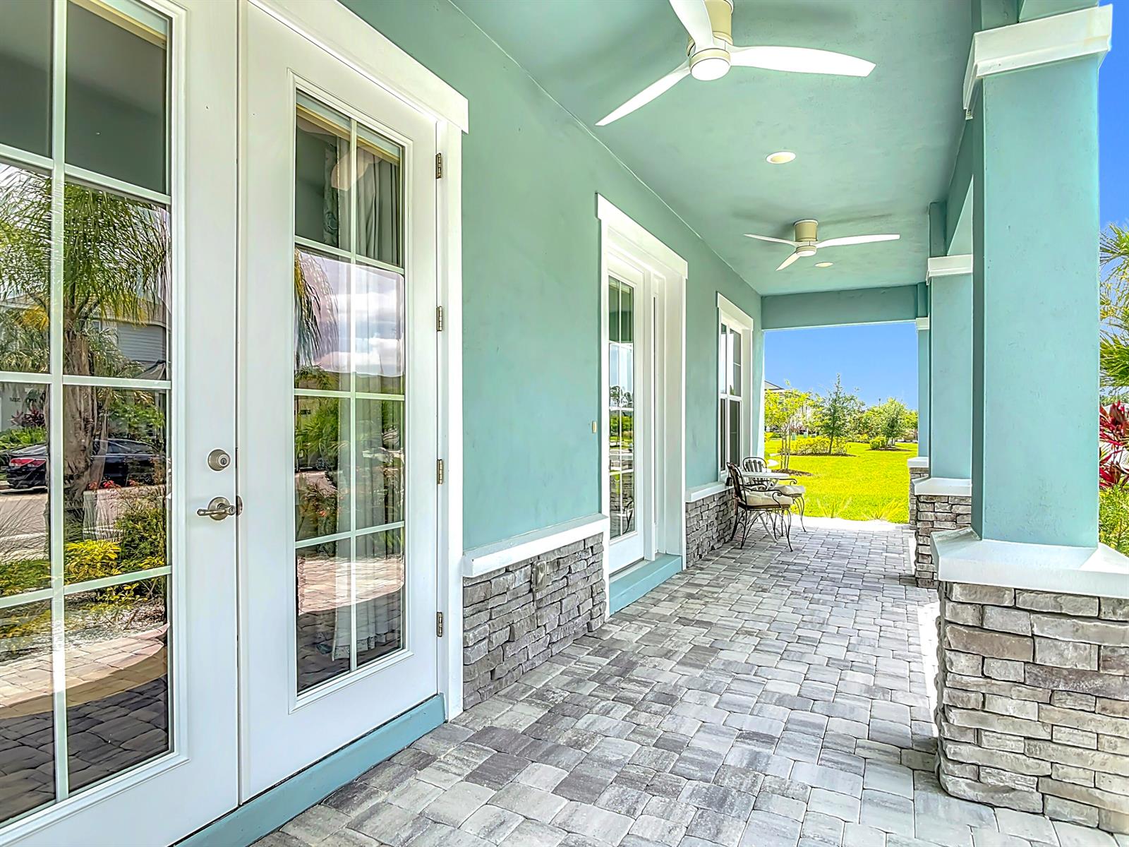 A covered patio features light blue walls, stone accents, paver flooring, and two ceiling fans — 3121 Portofino Boulevard, FL 32168, FL