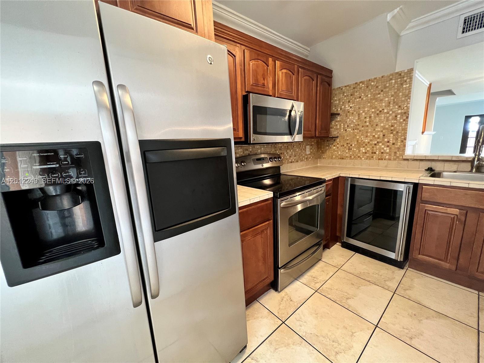 A kitchen features stainless steel appliances, wood cabinetry, and a mosaic tile backsplash — 1187 NW 124th Ave, Miami FL 33182, MIAMI, FL