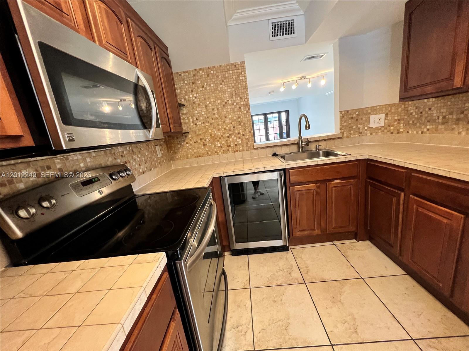 A kitchen features wood cabinets, tile countertops, a stainless steel microwave, and a wine cooler — 1187 NW 124th Ave, Miami FL 33182, MIAMI, FL