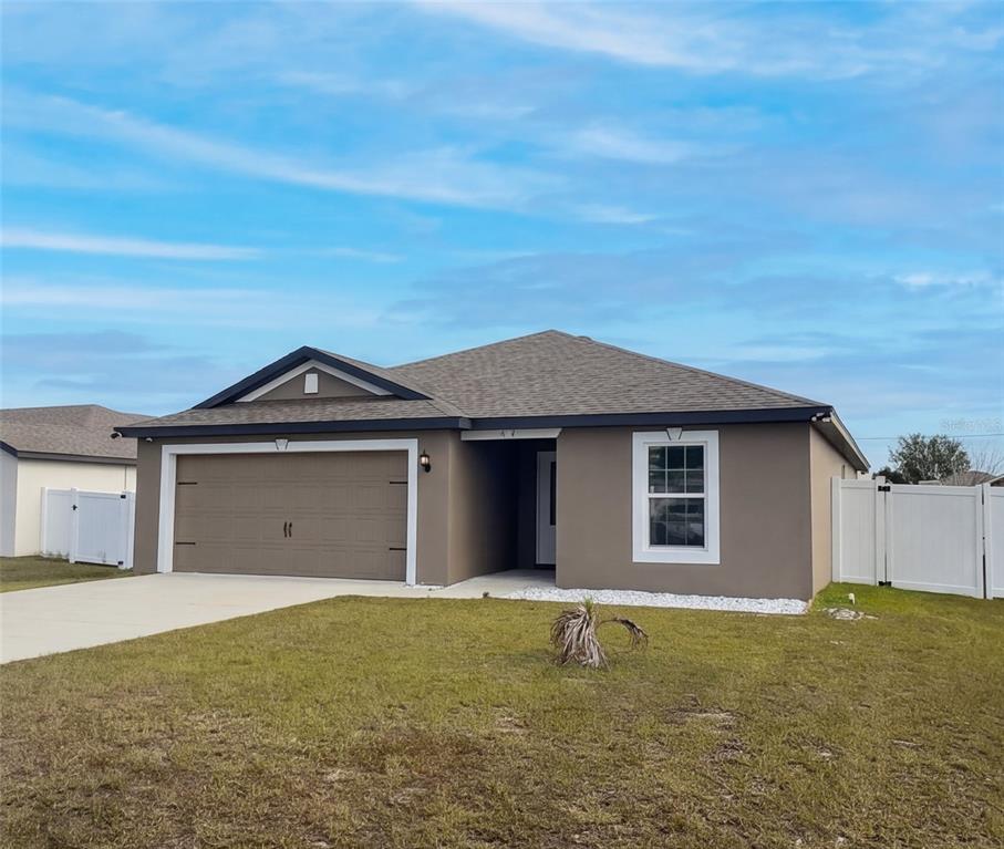 A single-story house with a tan stucco exterior, a two-car garage, and white vinyl fencing — 313 CAMELLIA COURT, POINCIANA, FL