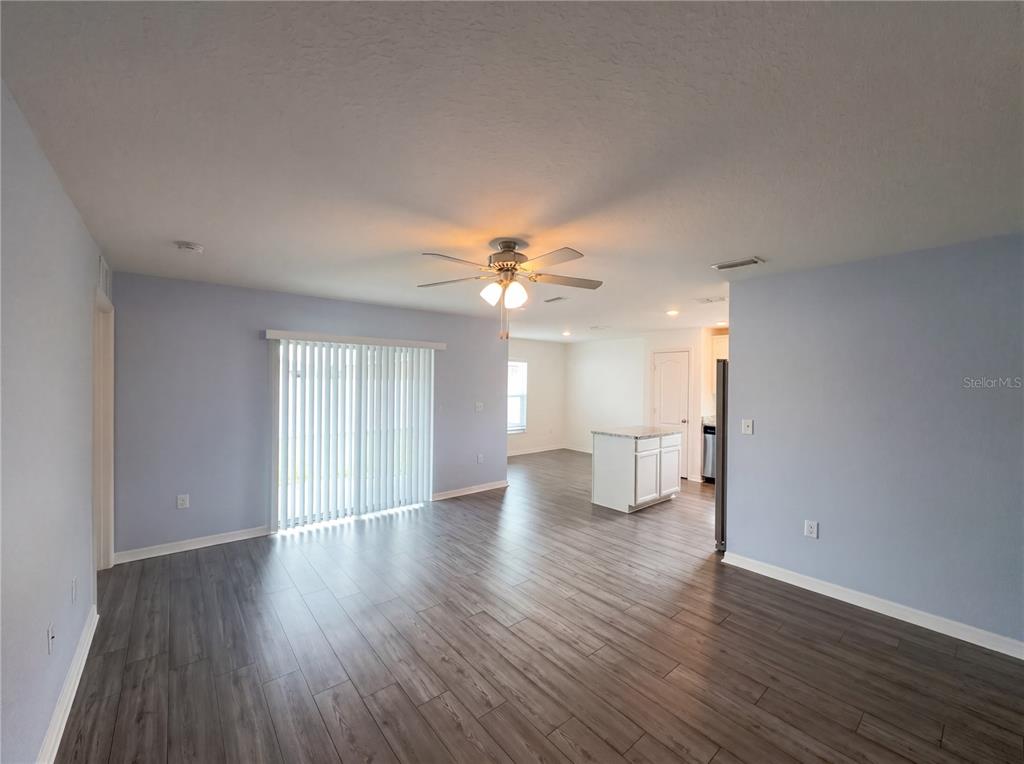 A living room with light blue walls, wood-look flooring, a ceiling fan, and sliding doors — 313 CAMELLIA COURT, POINCIANA, FL