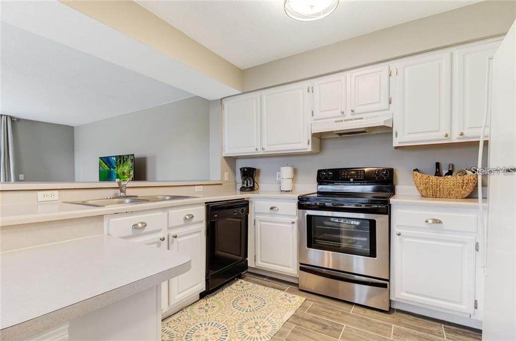A kitchen features white cabinets, stainless steel appliances, a black dishwasher, and light countertops — 13953 FAIRWAY ISLAND DRIVE UNIT 621, ORLANDO, FL