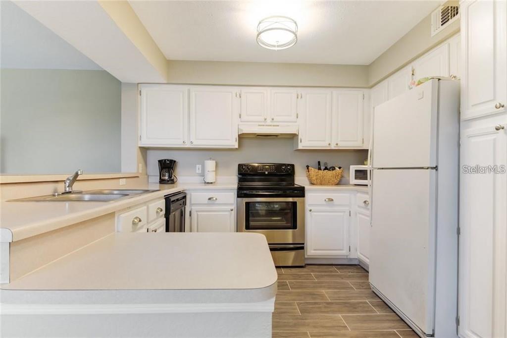 A kitchen features white cabinets, stainless steel appliances, a white refrigerator, and wood-look tile flooring — 13953 FAIRWAY ISLAND DRIVE UNIT 621, ORLANDO, FL