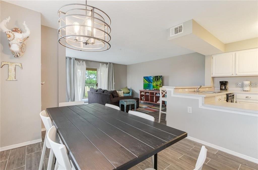 A dining area with a dark wood table leads into an open living room and kitchen — 13953 FAIRWAY ISLAND DRIVE UNIT 621, ORLANDO, FL