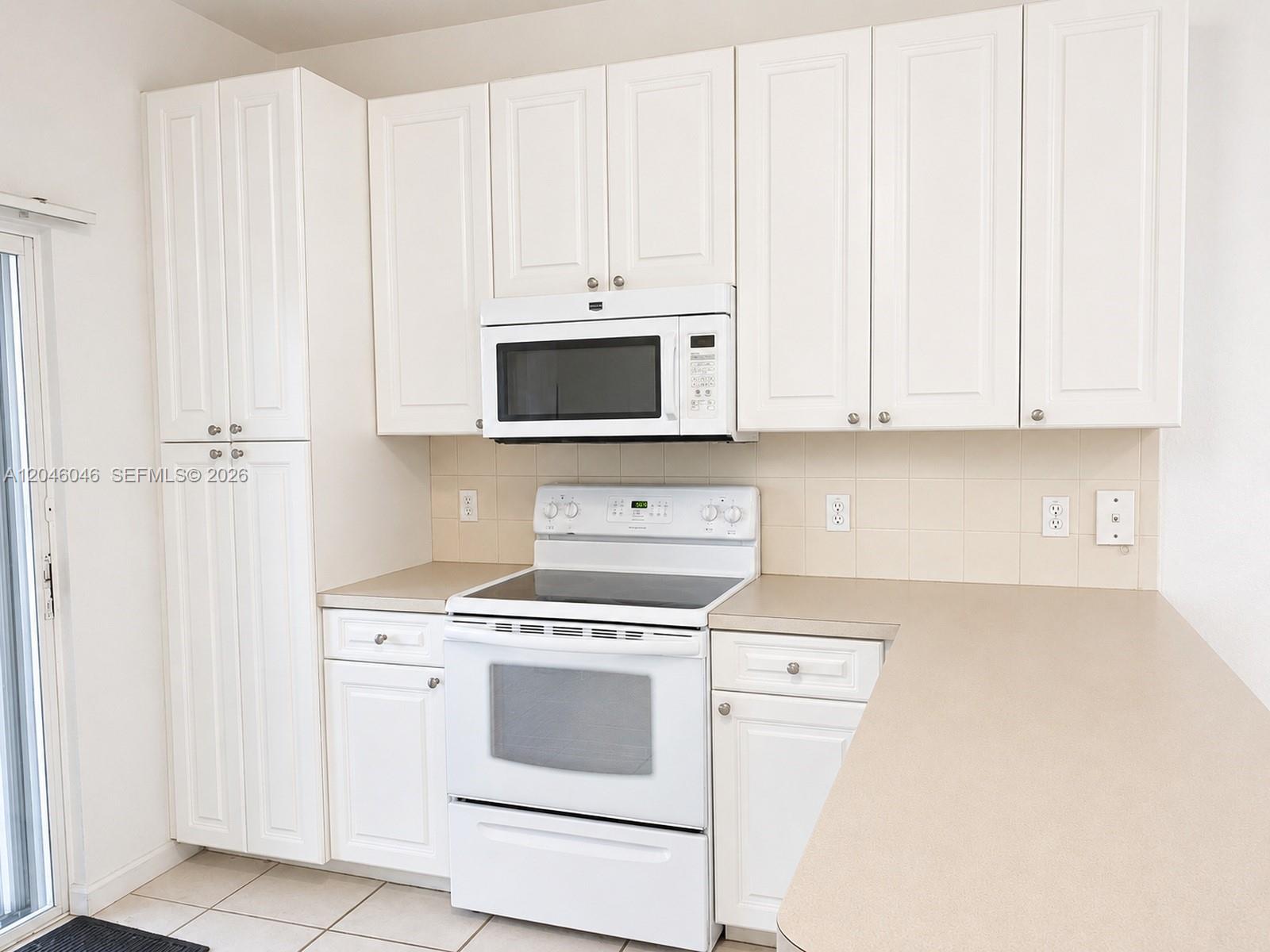 A kitchen features white cabinets, white appliances, and beige countertops against a tiled backsplash — 4950 Washington St # 4, Hollywood FL 33021, HOLLYWOOD, FL