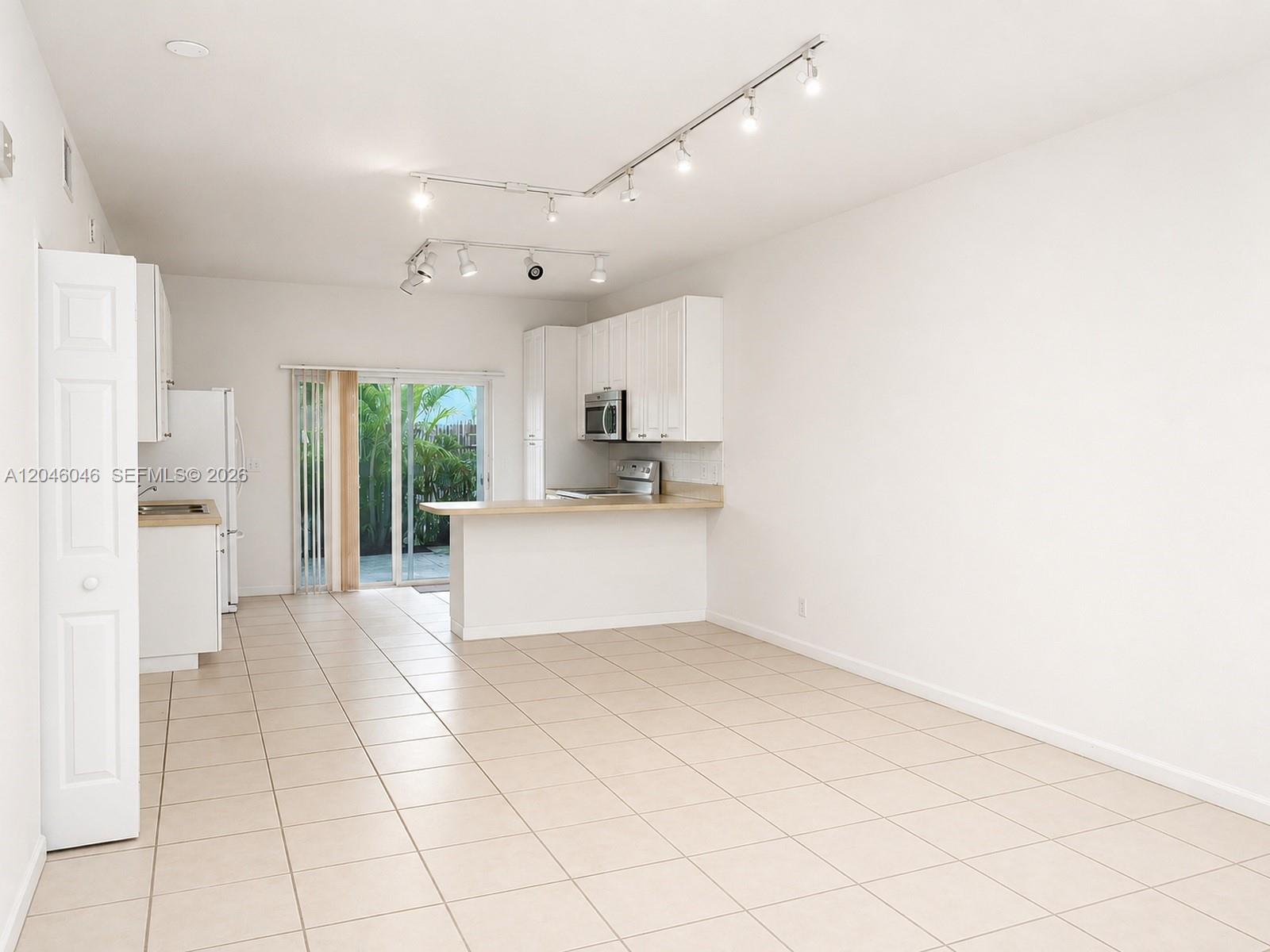 An open-concept kitchen and dining area features white cabinetry, tile flooring, and sliding glass doors — 4950 Washington St # 4, Hollywood FL 33021, HOLLYWOOD, FL