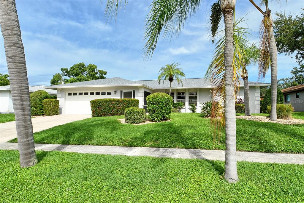 A single-story house with a white garage, manicured hedges, and palm trees in the yard — 6722 ROXBURY DRIVE, SARASOTA, FL