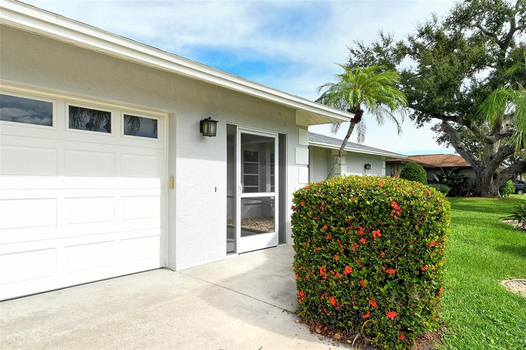 A white house exterior features a garage, a screen door, and a flowering hedge — 6722 ROXBURY DRIVE, SARASOTA, FL