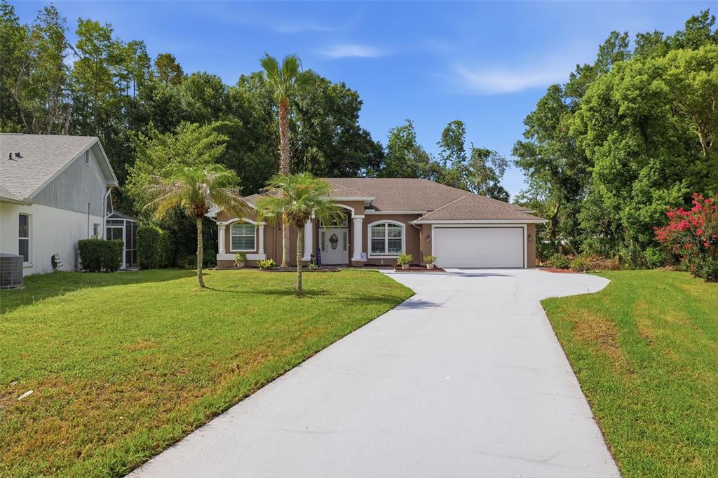 A single-story house with a tan exterior, white trim, a two-car garage, and palm trees — 4710 BASSWOOD STREET, LAND O LAKES, FL