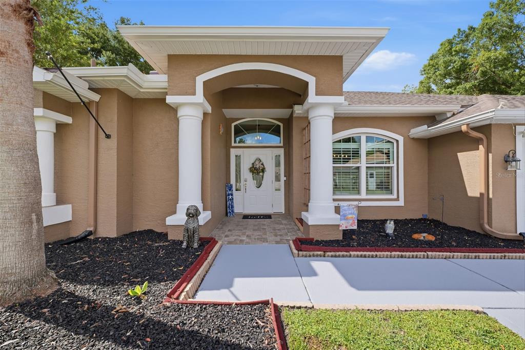 The exterior of a tan house features a covered entryway with white columns and a door — 4710 BASSWOOD STREET, LAND O LAKES, FL
