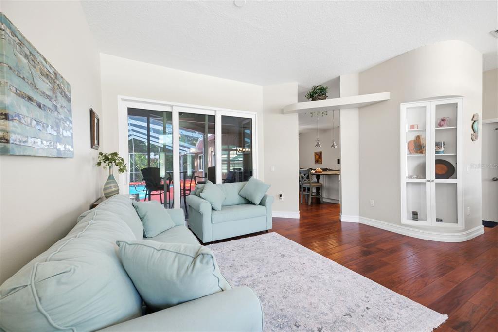 A living room with light blue furniture, hardwood floors, and a view of a pool — 4710 BASSWOOD STREET, LAND O LAKES, FL