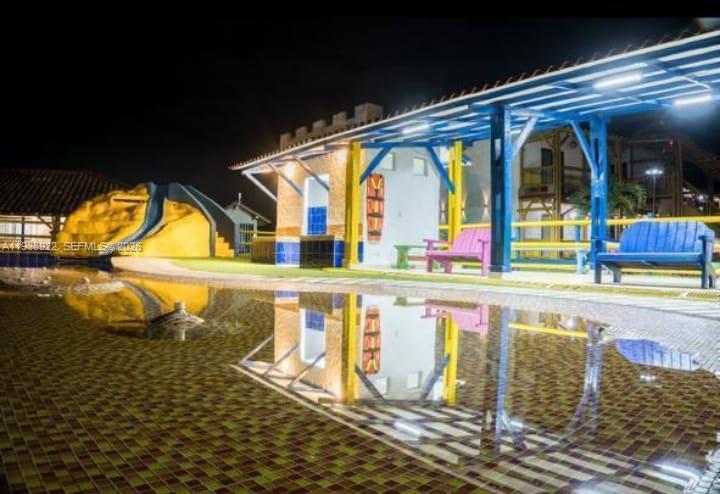 A swimming pool reflects a covered patio area with benches and a yellow water slide — Outside of Country, NO, NO