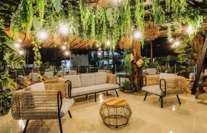 An outdoor lounge area features wicker chairs, a sofa, and hanging plants under string lights — Outside of Country, NO, NO