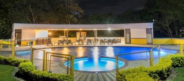 A swimming pool with a surrounding fence and a covered patio area at night — Outside of Country, NO, NO