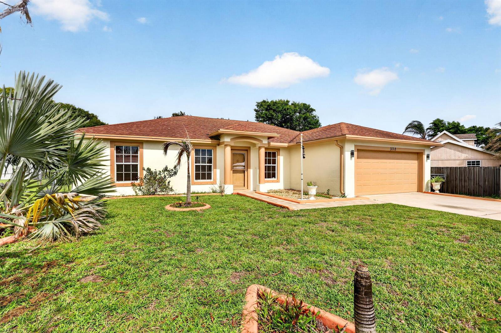A single-story house with a tan exterior, brown roof, and a two-car garage — 372 NW Hogan Street, FL 34983, FL