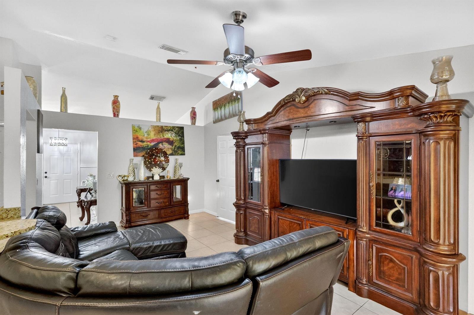 A living room features a large dark wood entertainment center, a black leather sectional, and tile flooring — 372 NW Hogan Street, FL 34983, FL