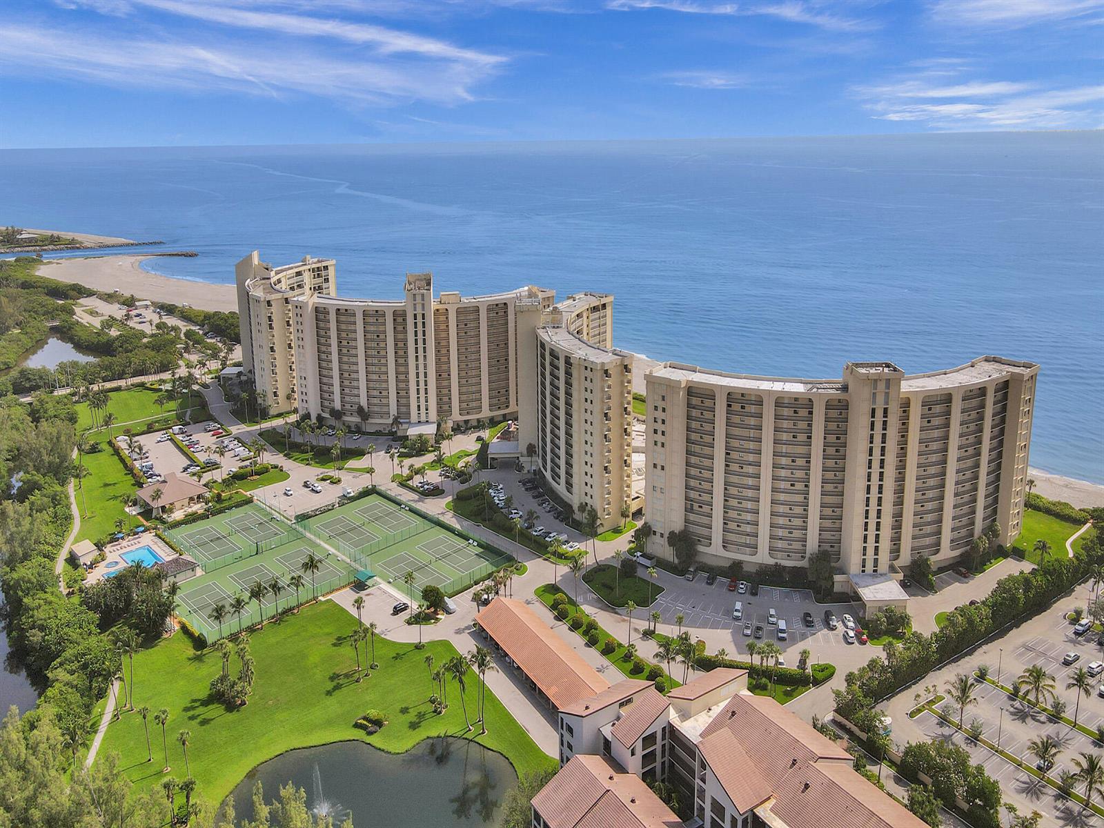 An aerial view shows two large curved residential buildings near a beach with tennis courts — 300 Ocean Trail Way # 306, Jupiter FL 33477, JUPITER, FL