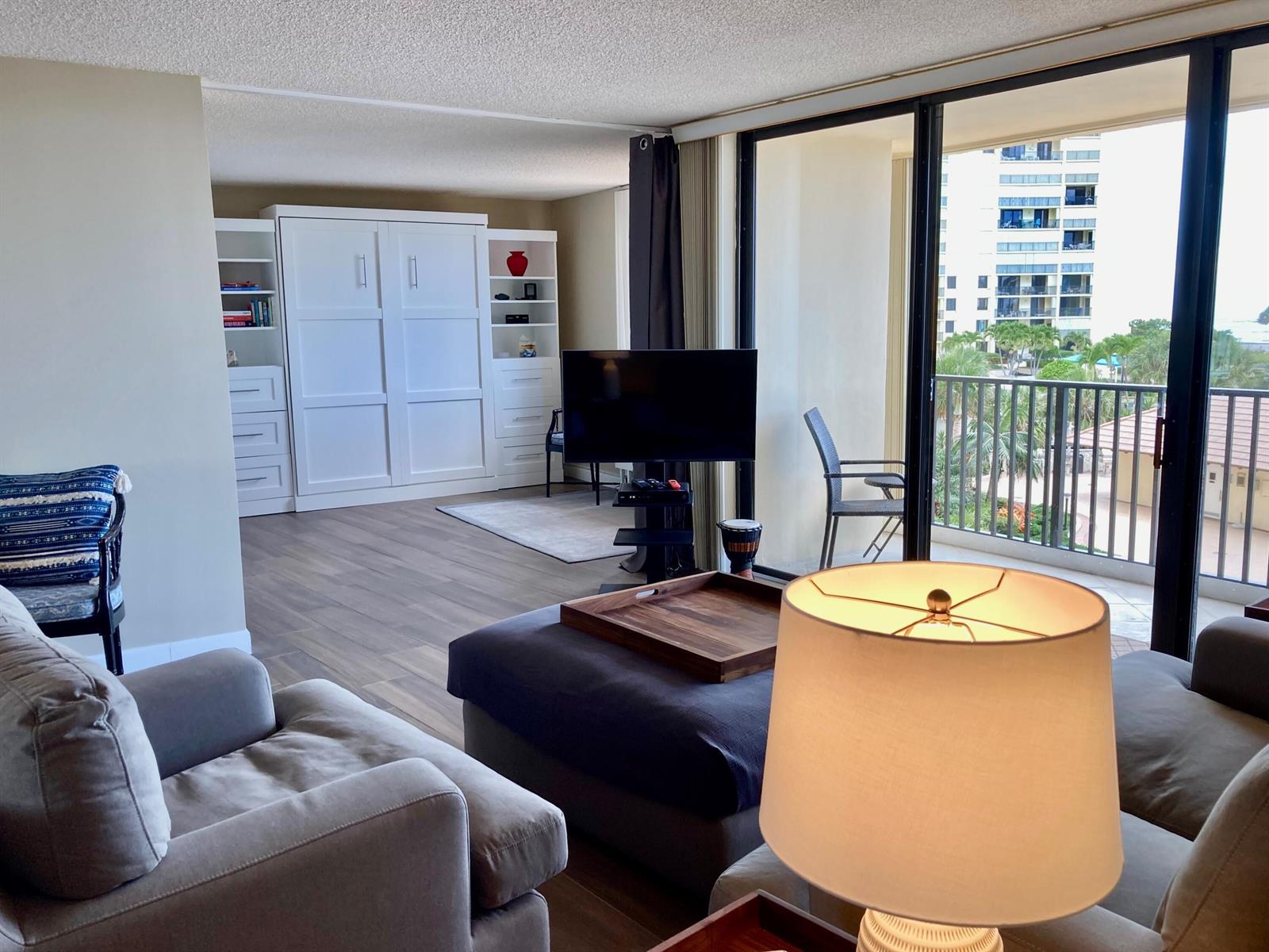 A living room with a Murphy bed, television, and a balcony overlooking a nearby building — 300 Ocean Trail Way # 306, Jupiter FL 33477, JUPITER, FL