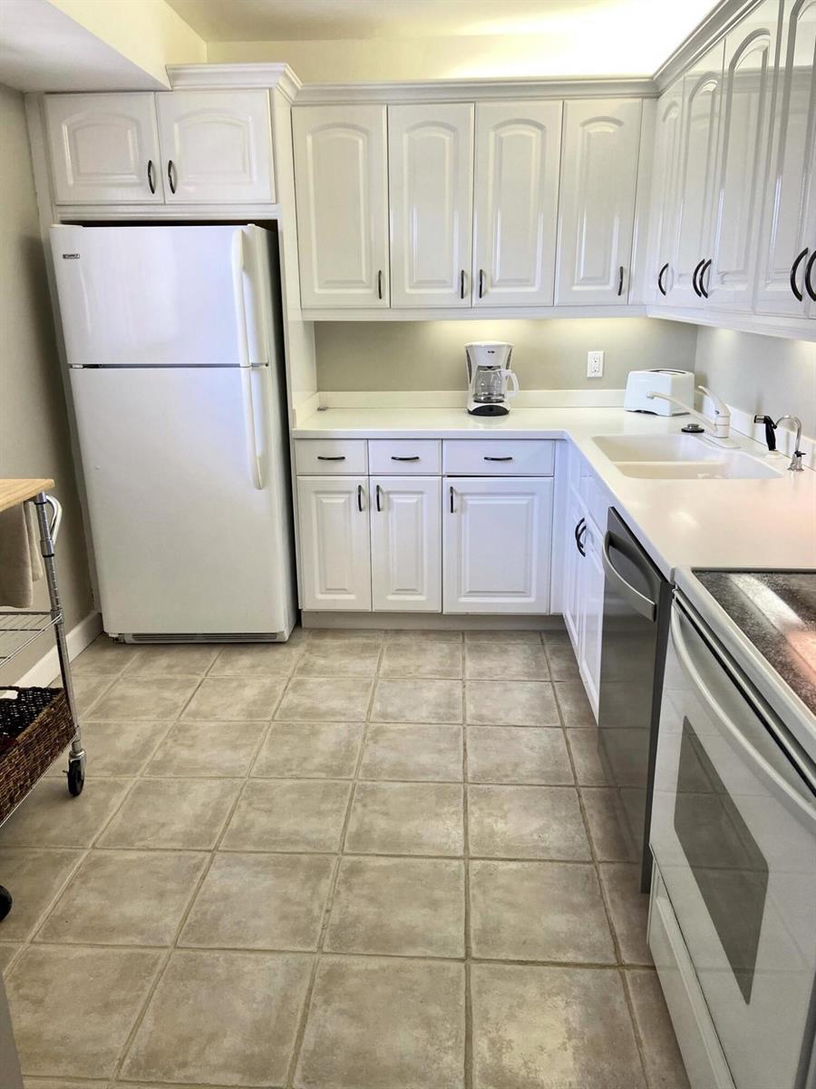 A kitchen features white cabinets, white appliances, a double sink, and light-colored tile flooring — 300 Ocean Trail Way # 306, Jupiter FL 33477, JUPITER, FL