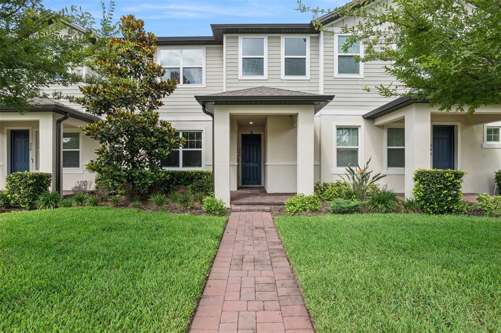 A multi-unit townhouse exterior features beige siding, brick walkways, and a manicured front lawn — 942 LEGACY WINDS WAY, CASSELBERRY, FL