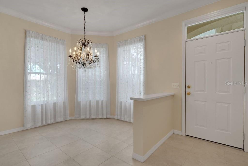 A dining area features tile flooring, a crystal chandelier, and a white front door — 684 GRASSLANDS VILLAGE CIRCLE, LAKELAND, FL