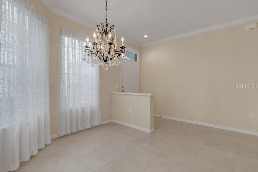 A dining room with tile flooring, a crystal chandelier, and a half-wall near the entrance — 684 GRASSLANDS VILLAGE CIRCLE, LAKELAND, FL