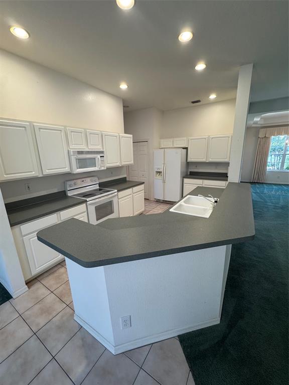 A kitchen features white cabinets, dark countertops, a white stove, and a peninsula sink — 7884 KAVANAGH COURT, SARASOTA, FL