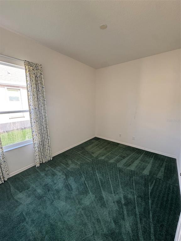 An empty bedroom features white walls, a single window with floral curtains, and green carpeting — 7884 KAVANAGH COURT, SARASOTA, FL