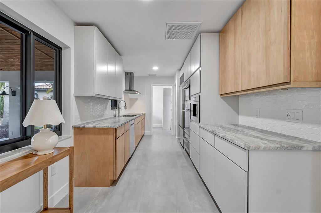 A modern galley kitchen features light wood cabinets, white upper cabinets, and marble-patterned countertops — 15180 LYNEBURG AVENUE, PORT CHARLOTTE, FL